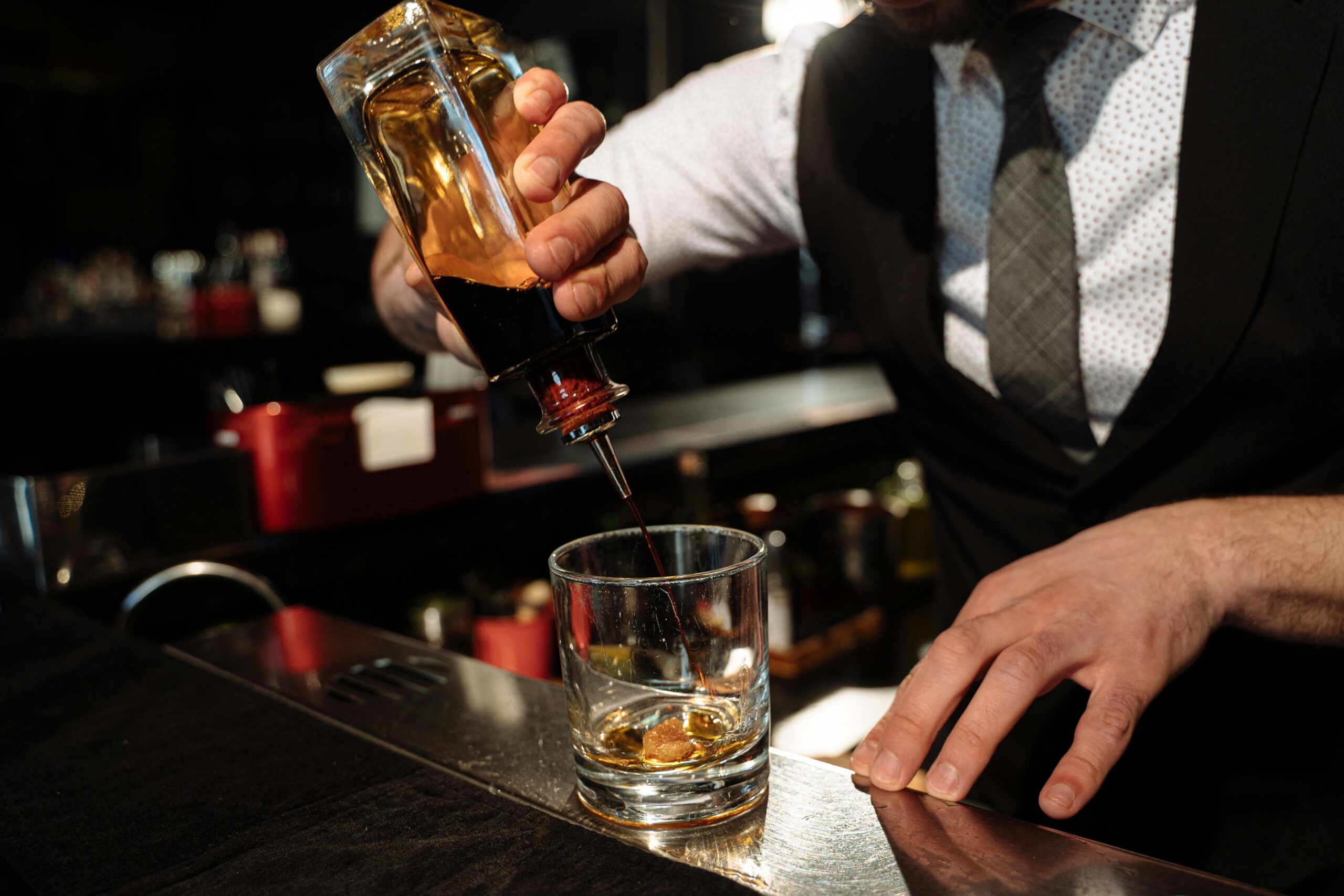 Close-up of bartender pouring whiskey into a glass at a bar counter.